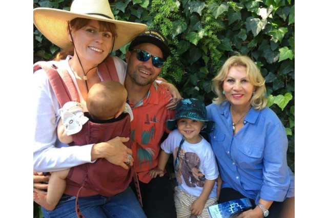 Family photo with a dad in the middle, his wife on his right with an infant in her lap, his toddler son to his left, and the grandmother next to him.